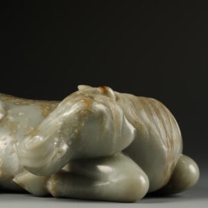 A celadon jade reclining horse with brown mottling (Late Ming dynasty, 17th century)