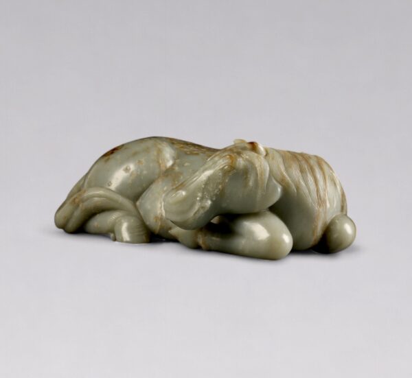 A celadon jade reclining horse with brown mottling (Late Ming dynasty, 17th century)